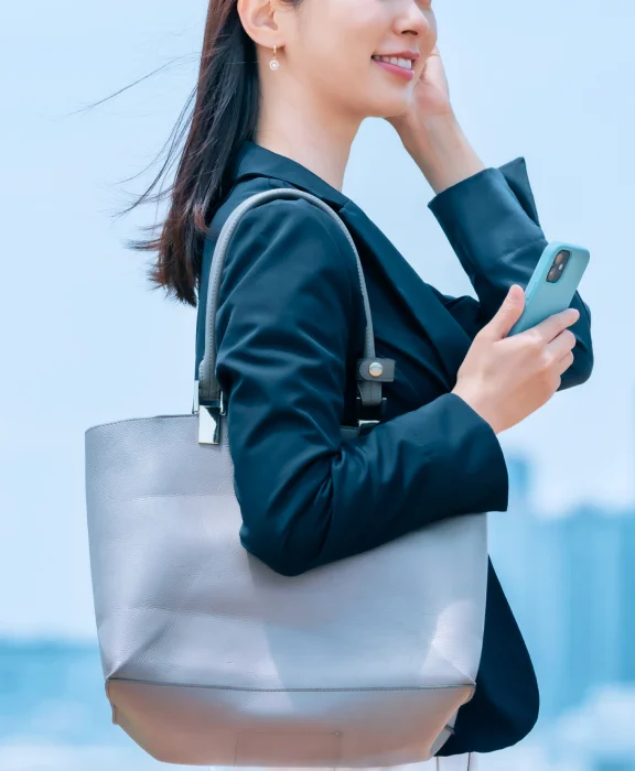 肩にカバンをかけて、右手にスマホを持った女性が歩いている。